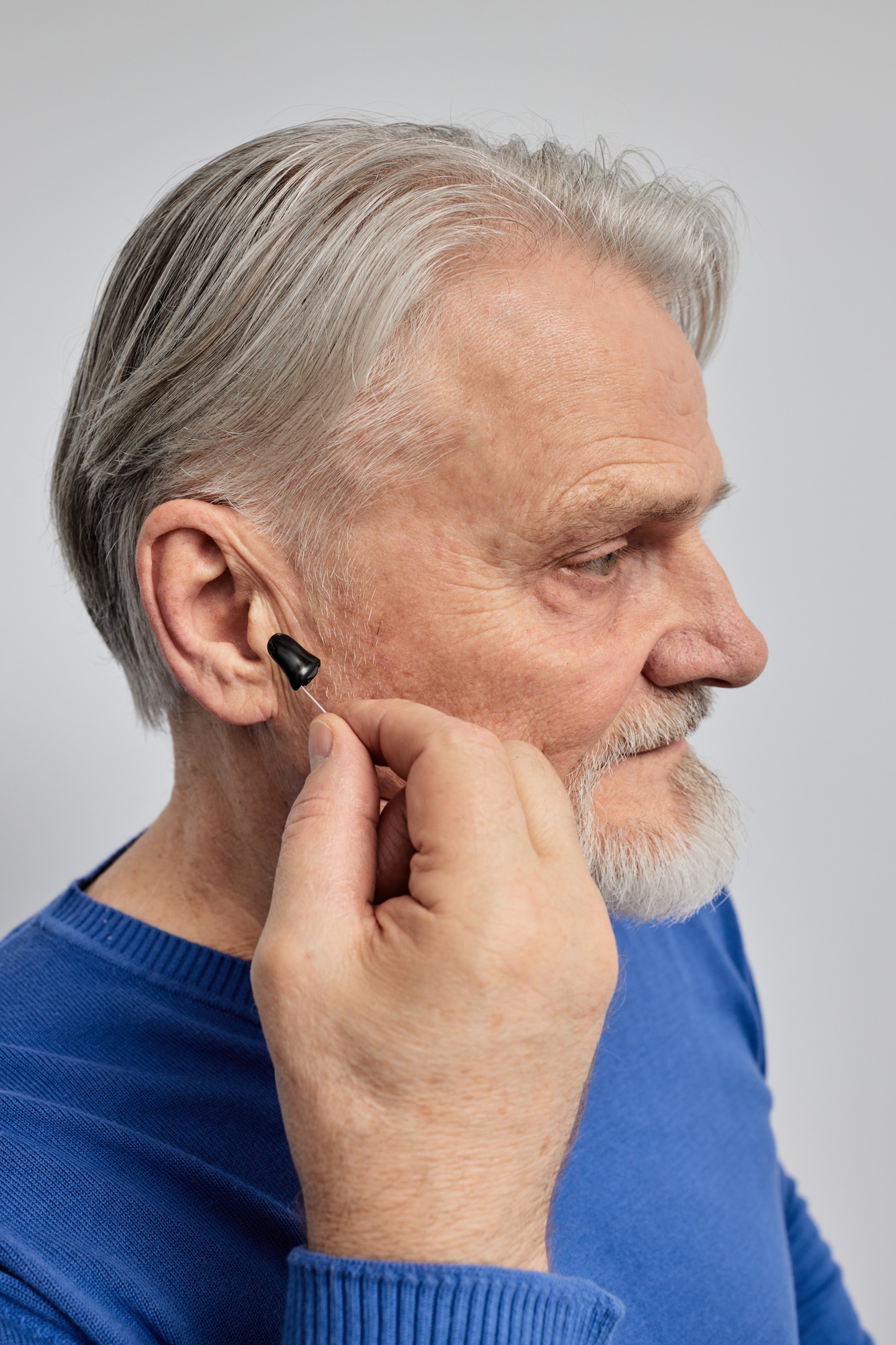 Hearing impaired senior man holding his in-the-ear hearing aid. Hearing aids