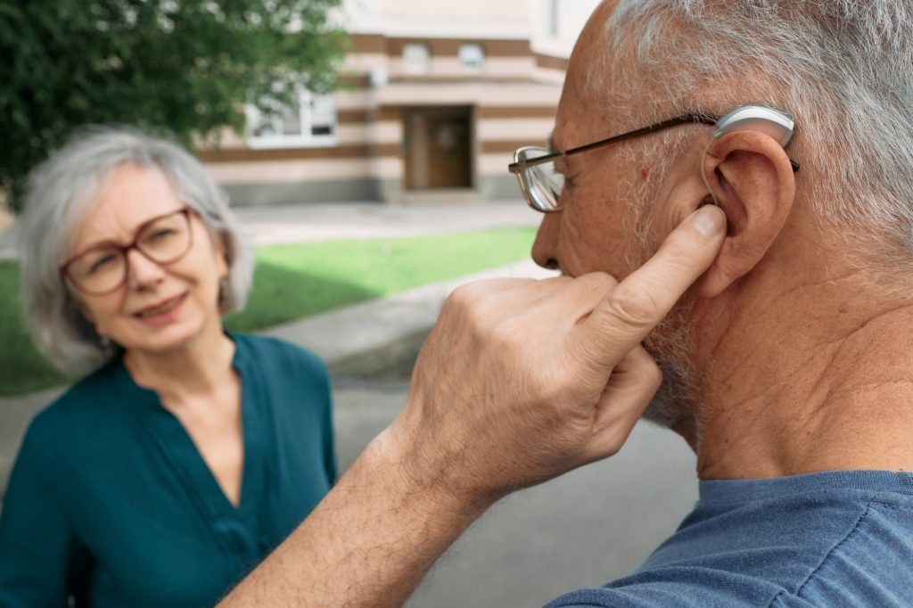 Mature man with a hearing impairment uses a hearing aid to communicate with his female senior